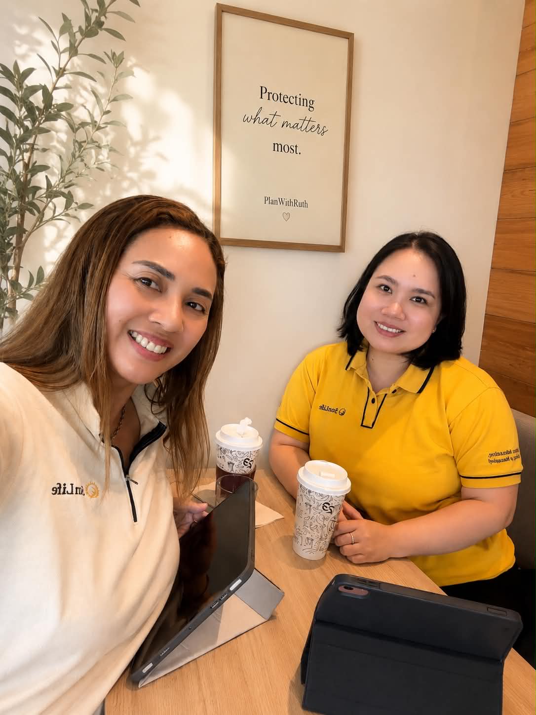 Ruth Abestilla meeting a Sun Life teammate over coffee, tablets on the table beneath a framed PlanWithRuth print