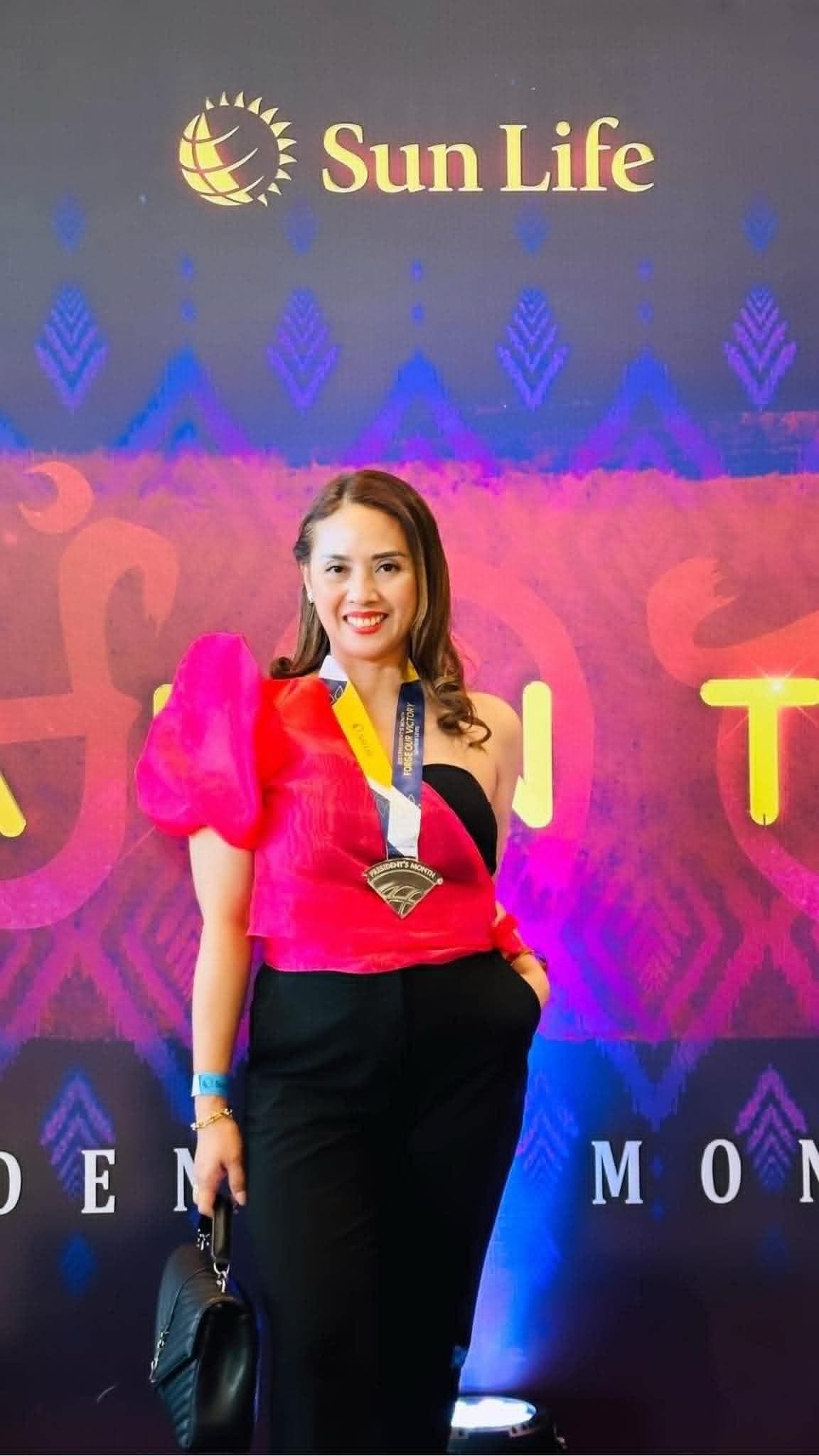 Ruth Abestilla wearing a recognition medal in front of a Sun Life backdrop